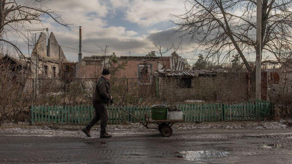 A man pushes a trolley with a coal container to his flat, passing war-damaged buildings