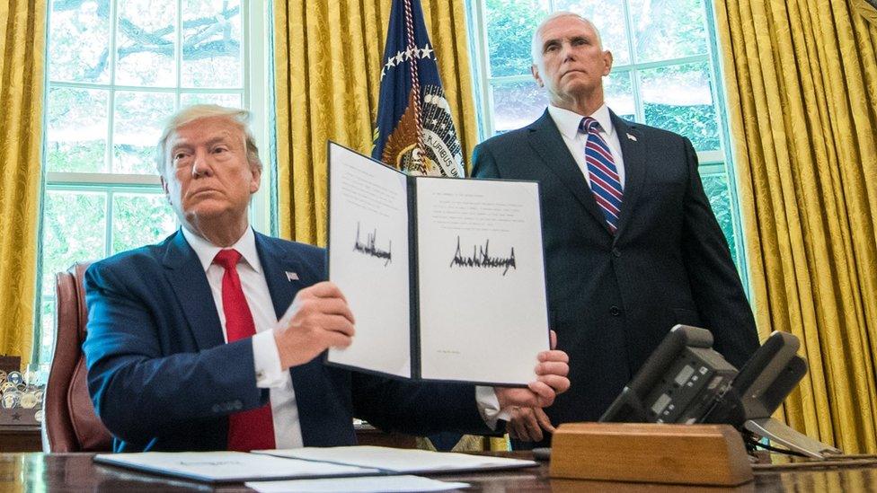 US President Donald J. Trump holds up a copy of an executive order in the Oval Office