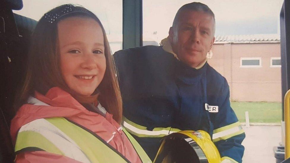 Mike in his firefighter's uniform with a young Beth in a fire engine