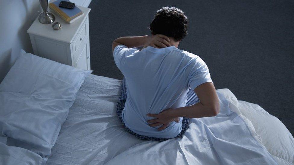 Man holding his back and neck on a bed