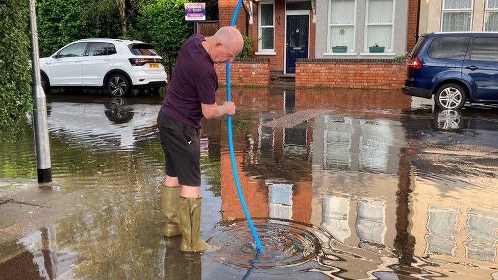 A man putting a pipe down a drain on the corner of Denmark Street, Bedford