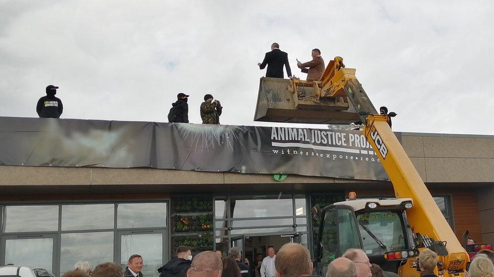 Men standing in JCB bucket speak to protestors on rooftop