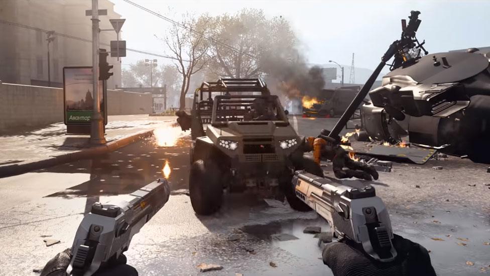 A first-person view shows the burning vehicles on a street, with the player's hands visible in-frame holding two pistols