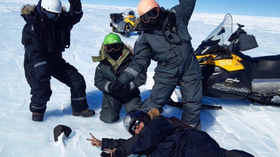 Team of scientists in snowsuits, pointing at meteorite