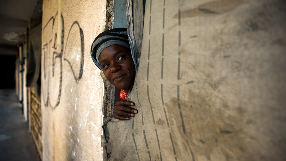 An unidentified woman peeks out of her room. With the doors and door frames removed, a fabric sheet serves as a makeshift door in the derelict San Jose building in Johannesburg, South Africa