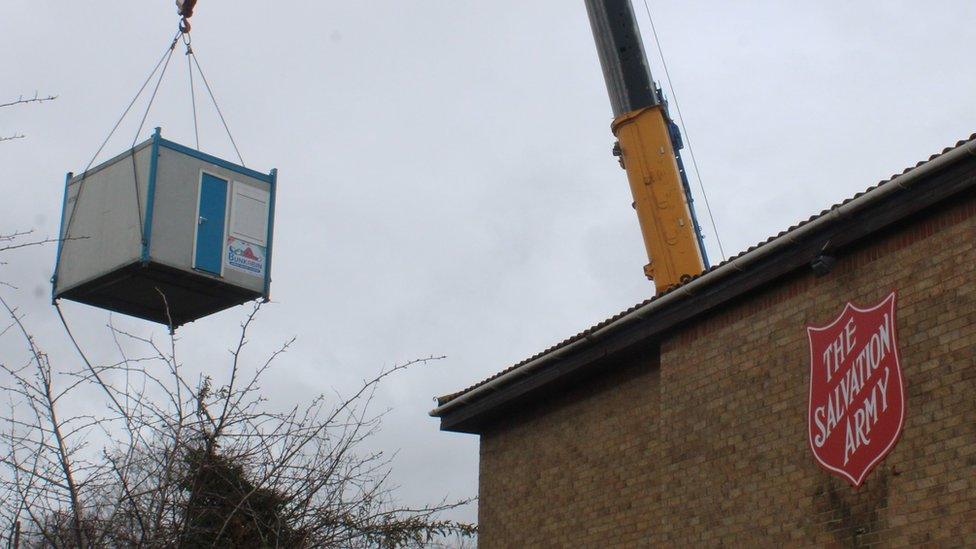 Crane lowering a sleeping pod next to a Salvation Army building