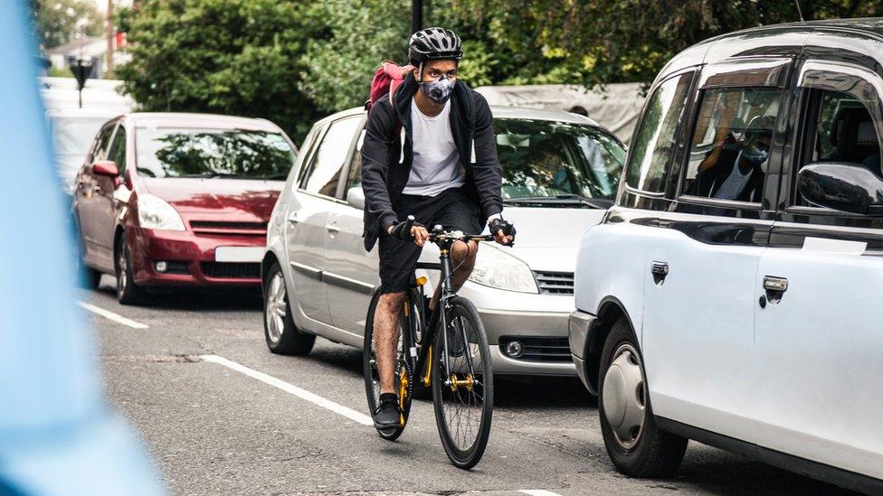 Cyclist commuter cycling through central London traffic while wearing a pollution mask.