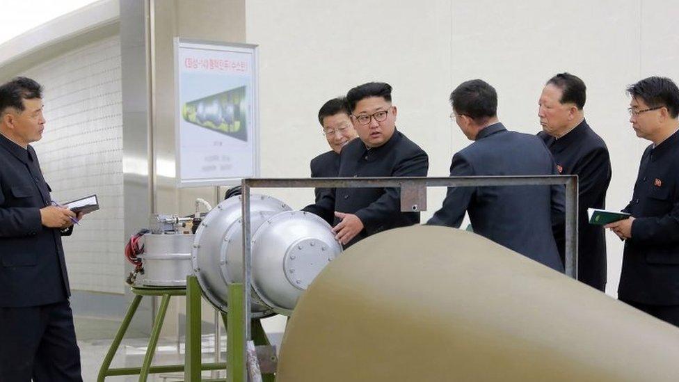 North Korean leader Kim Jong-Un (C) looking at a metal casing with two bulges at an undisclosed location