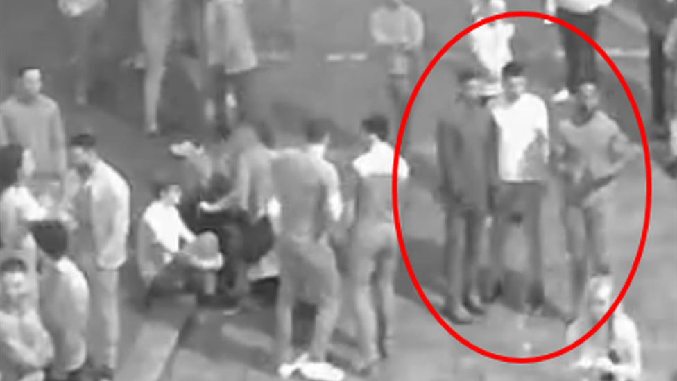 A CCTV image of a crowd in bvlack and white with three men circled in red