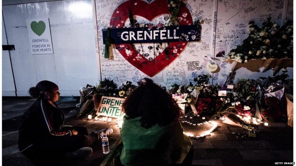 A woman seen standing in front of the flowers memorial at the foot of the Grenfell Tower