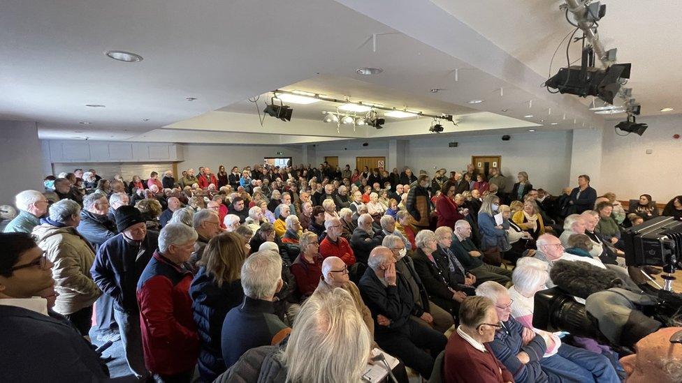 People sitting in a hall to discuss the closure of their GP surgery