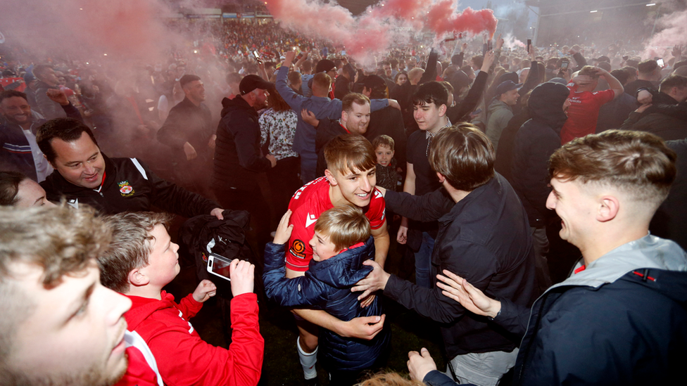 Wrexham's Max Cleworth celebrates with fans on the pitch after the match