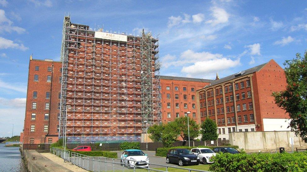 A block of red brick buildings on the banks of a river