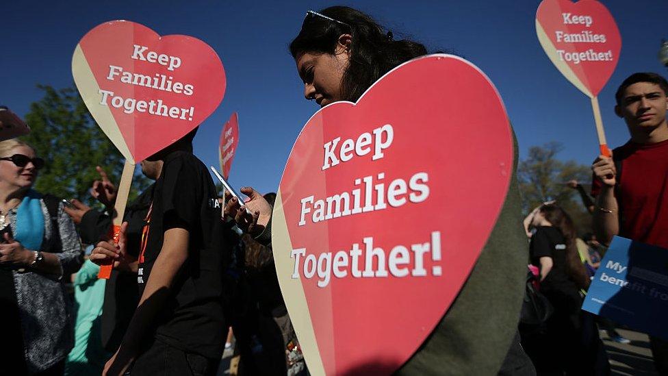 A woman holds a "keep families together" sign.