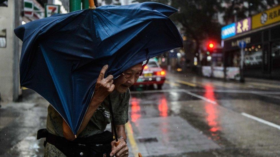 An elderly man man struggles with an umbrella in a Hong Kong city street