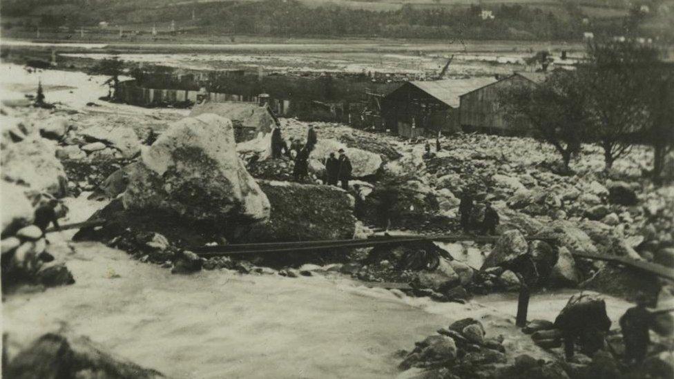 This photograph shows villagers using planks to cross Dolgarrog following the dam disaster.