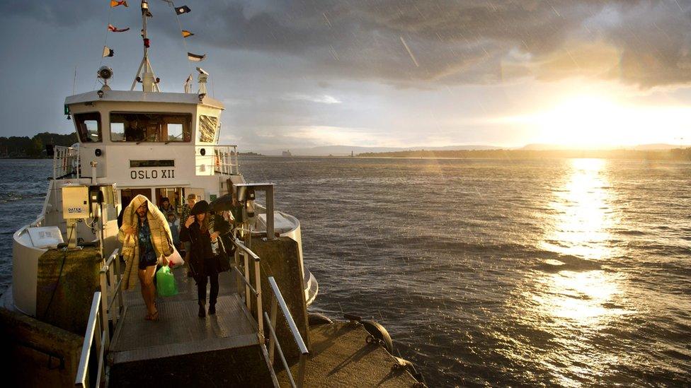 This file photo taken on August 24, 2012 shows tourists coming back from the Hovedoya island in the Oslo fjord during a rain shower as they disembark from a ferry in Oslo at sunset.