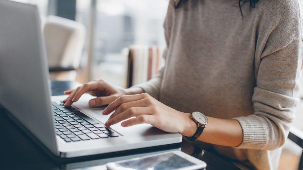 Woman sitting at a table typing on a laptop