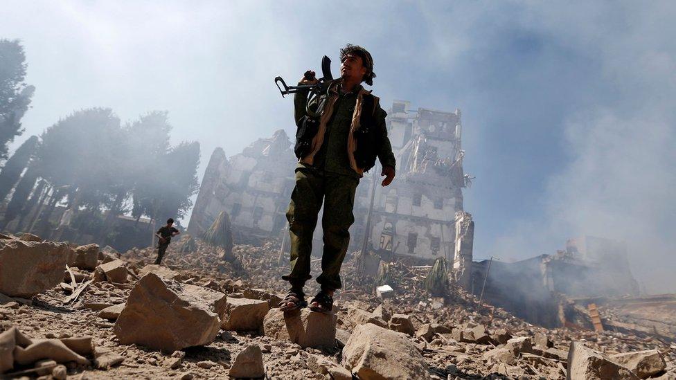 Houthi rebel fighter stands outside a presidential palace destroyed in a reported Saudi-led coalition air strike in Sanaa, Yemen (5 December 2017)