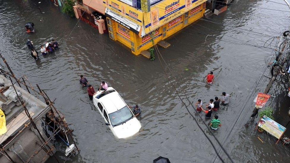 Indian residents attempt to push a vehicle through floodwaters as others wade past in Chennai on December 2, 2015.