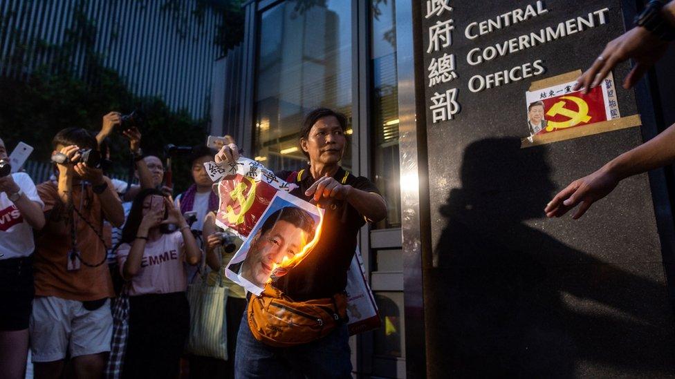 Pro-democracy activist Lui Yuk-lin (C) burns a portrait of Chinese President Xi Jinping outside the Central Government Offices after attending a protest march in Hong Kong on July 1, 2018