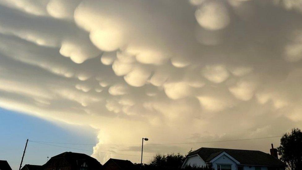 Dark clouds overhead a street, with bulges of sunlit cloud underneath them