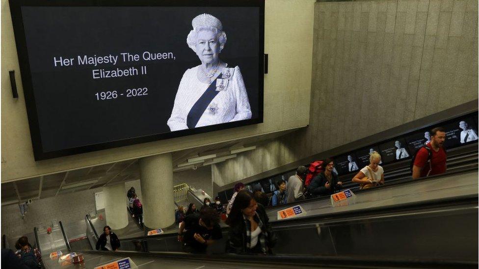 Commuters pass beneath a tribute image of Queen Elizabeth II as they travel through Kings Cross train station