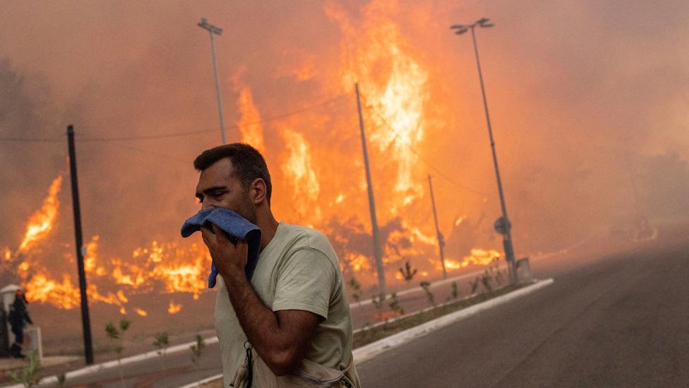 A volunteer covers his face to protect himself from the smoke, as a wildfire burns in the village of Hasia, near Athens, Greece