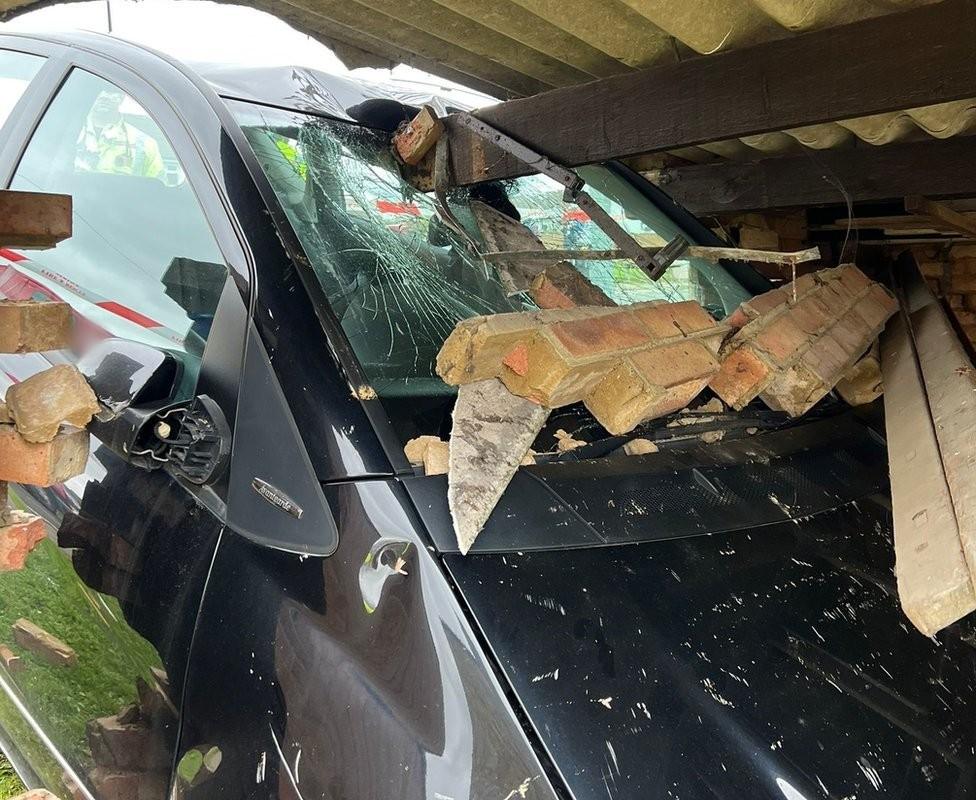 A damaged car that has smashed through a brick wall