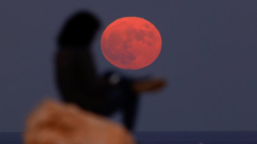 Bright red moon rising behind the silhouette of a woman