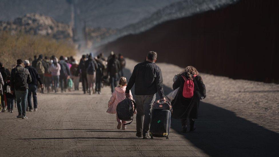 Asylum seeking migrants wait to be processed by the US Border Patrol after crossing from Mexico at a makeshift camp next to the US border wall on December 13, 2023 in Jacumba Hot Springs, California