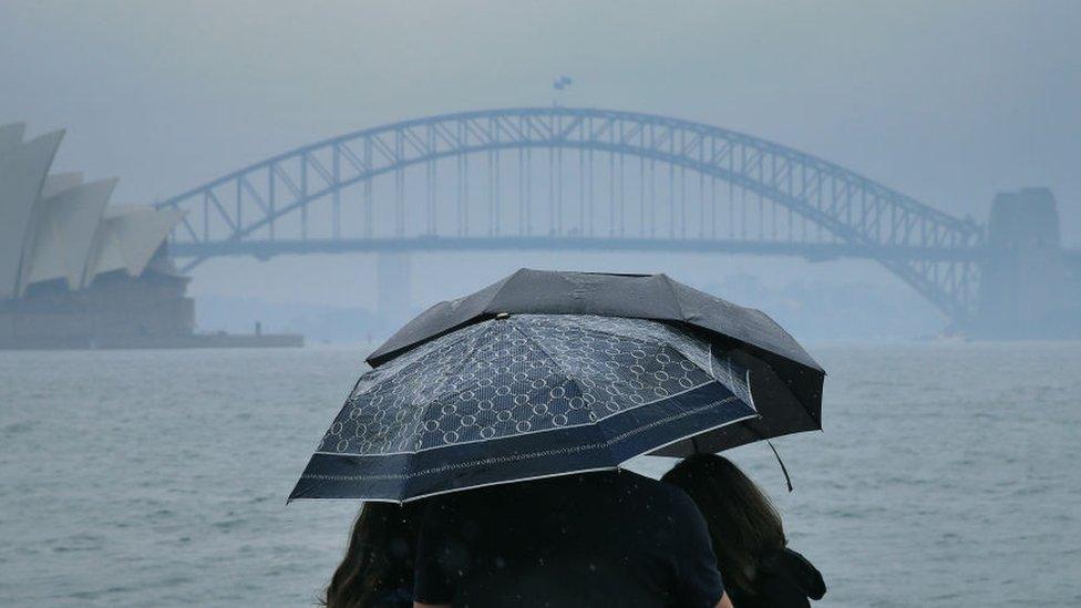 Tourists are seen looking at The Sydney Harbour Bridge in the rain