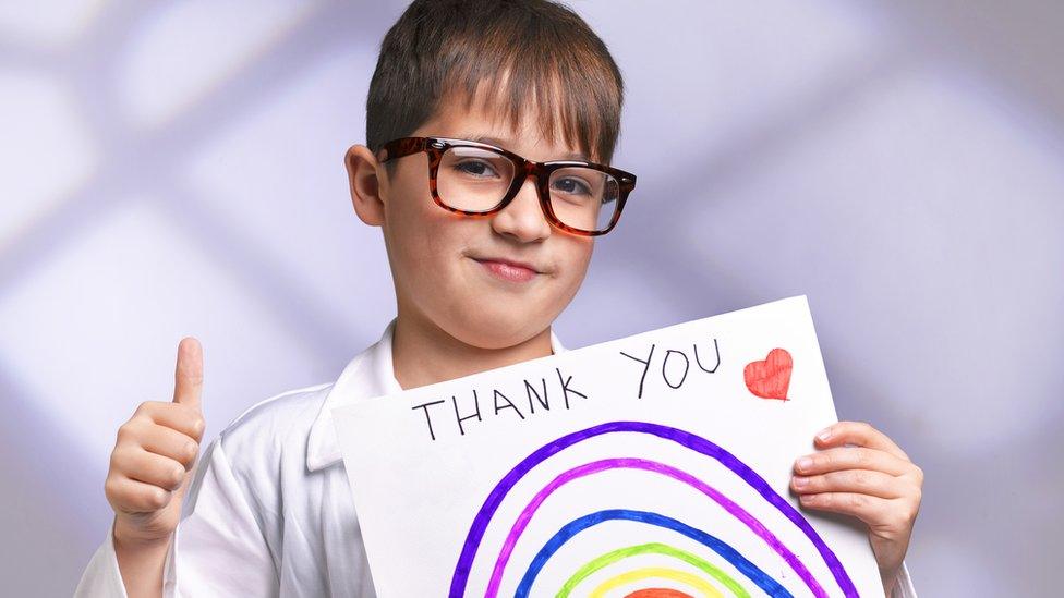 Boy with thumb up and holding a sign with a rainbow on and the words thank you