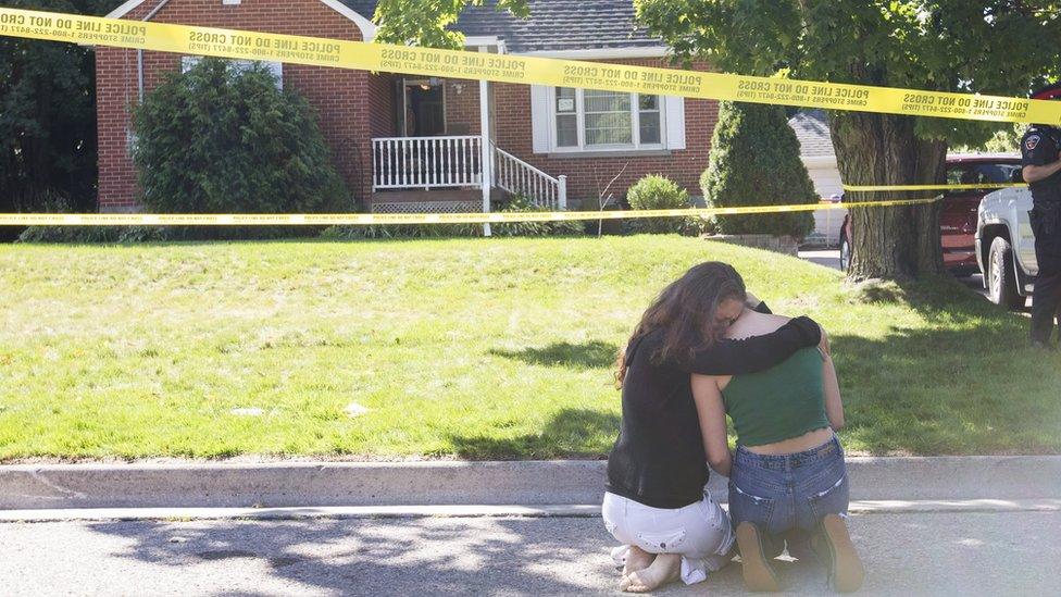 Two women console each other outside the house where the shooting took place