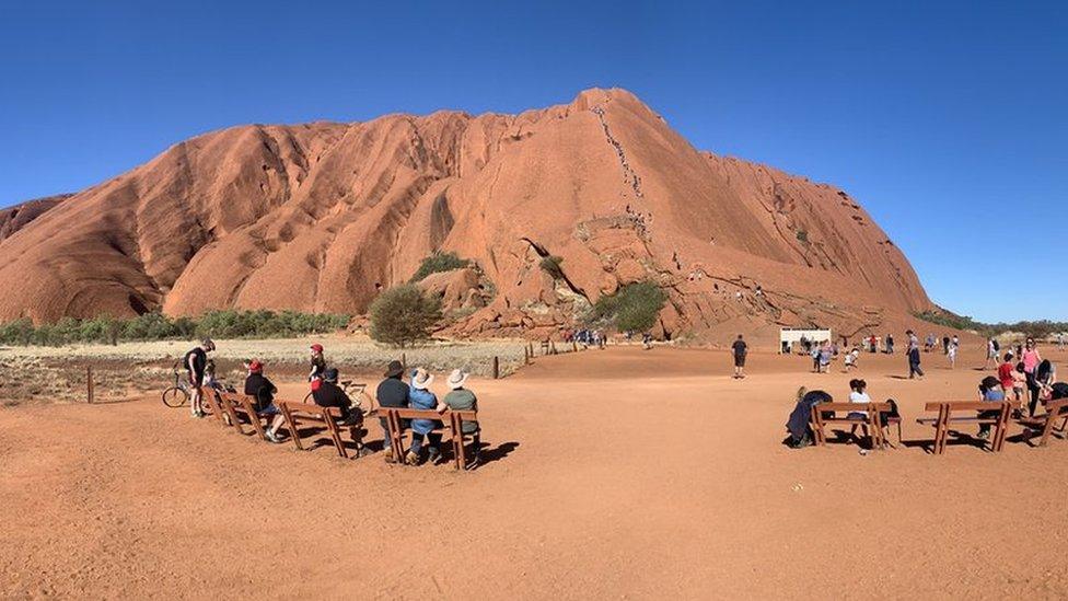 Locals watch on as tourists climb Uluru