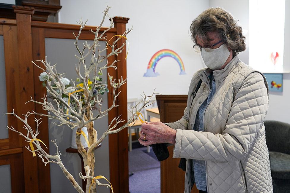 A woman ties a yellow ribbon to a memorial tree in a church