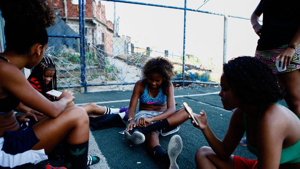 One of the girls, centre, fixes her shoe as the girls talk and check their phones after training