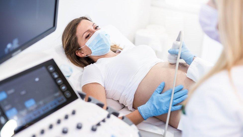 Pregnant woman wearing surgical mask and gloves having ultrasound