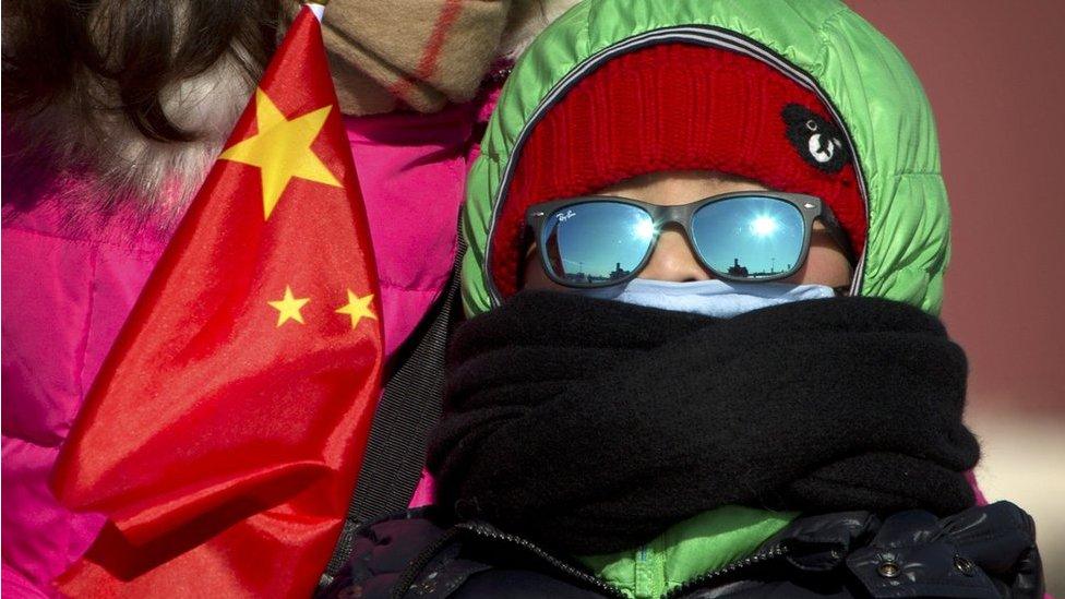 A boy in heavy winter clothing holds a Chinese flag as he stands in Tiananmen Square in Beijing, Saturday, 23 January 2016