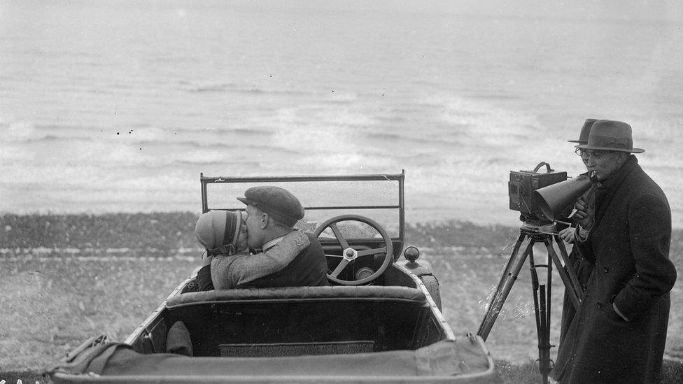 A couple in an open car locked in a passionate embrace for a scene in the film, The Thrill, being shot in 1926