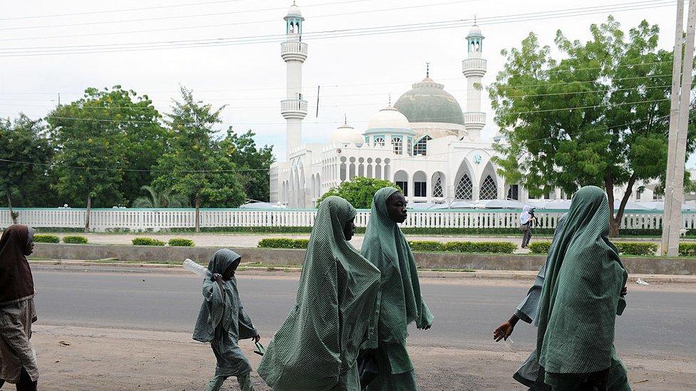 Students in hijabs walking past a mosque