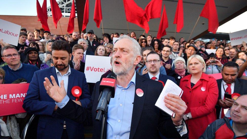 Corbyn at the front of a rally, with people holding 'vote Labour' signs