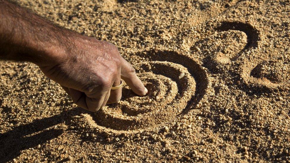 A close up of an Aboriginal man's hand drawing the dreamtime stories in the dirt