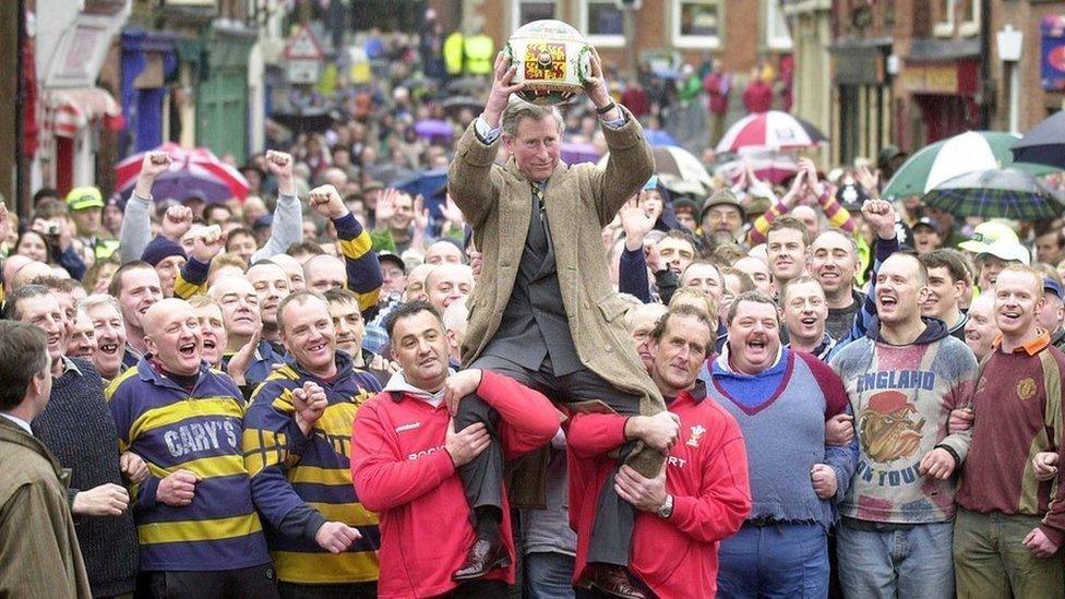 Prince Charles being lifted up holding the ceremonial ball before starting the ancient Royal Shrovetide Football game, in Ashbourne, Derbyshire. Holding the Prince shoulder-high were Dougie Souter and Mark Harrison (right of Prince with dark hair).