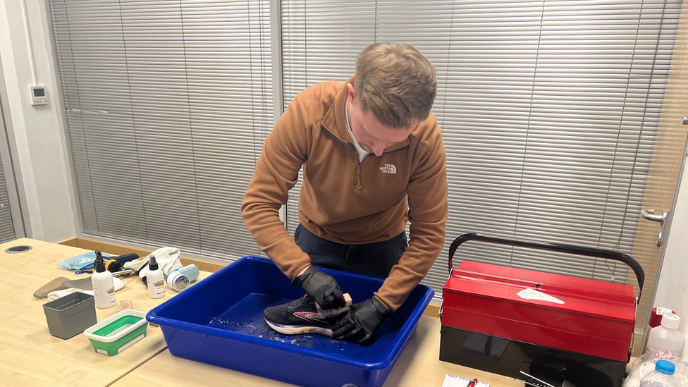 Liam Wood restoring a pair of trainers on a wooden table, surrounded by cleaning equipment