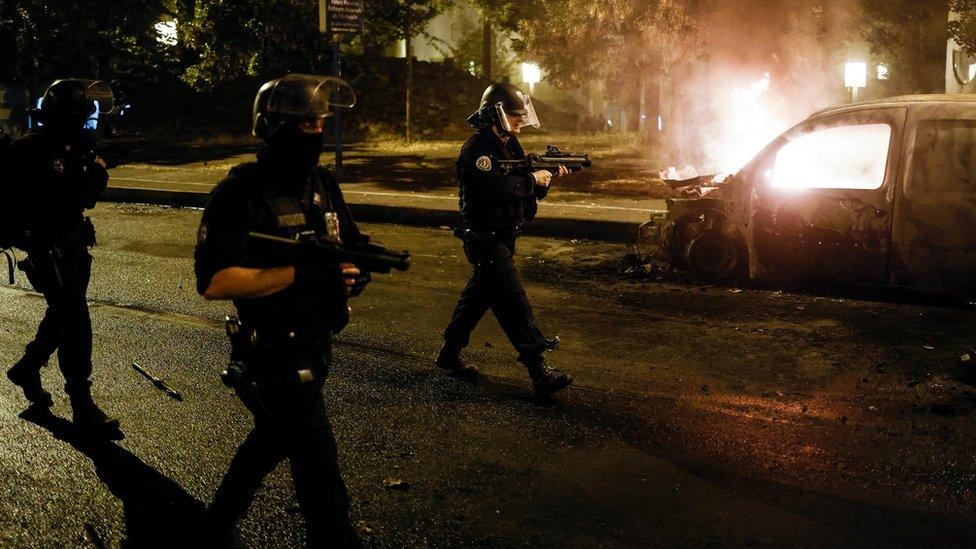 police-walk-past-burning-car-in-Nanterre.