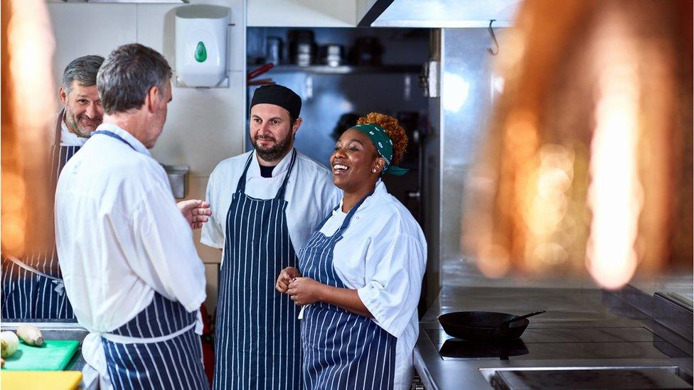 Colleagues working and talking in restaurant kitchen.