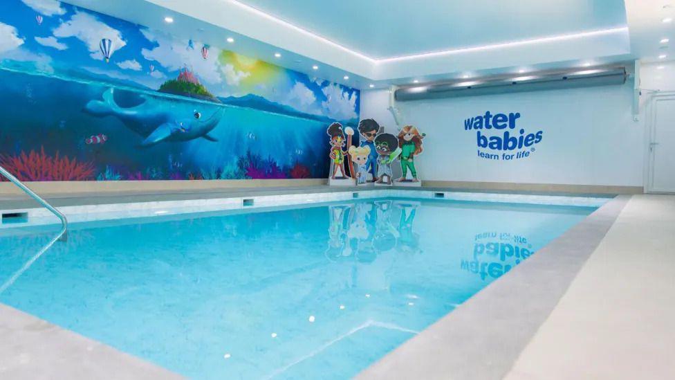 A swimming pool with a 'Water Babies' logo on the wall