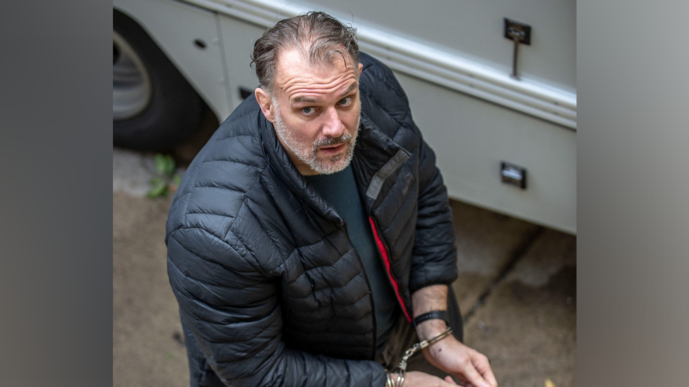 A view from above of Paul Whitehurst wearing handcuffs and a black puffer coat