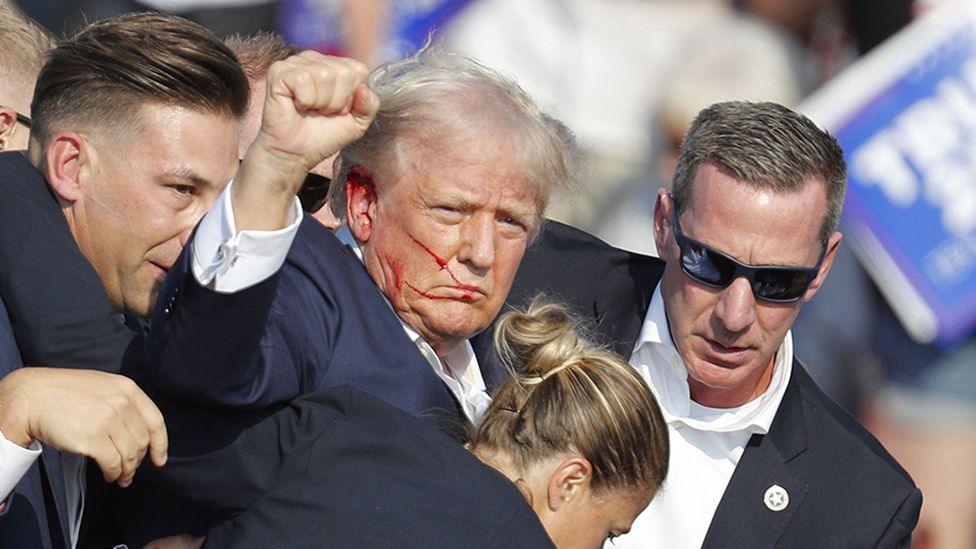 Trump raises fist as he is guided off stage